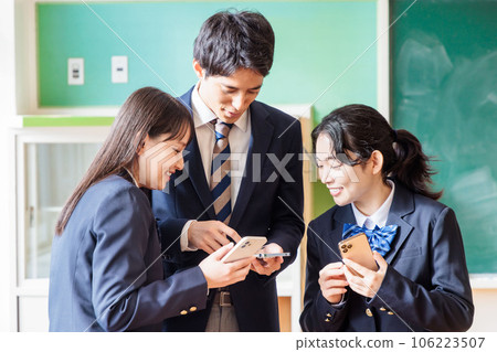 男女高中生在教室裡一邊看著同學和智能手機一邊交談 106223507