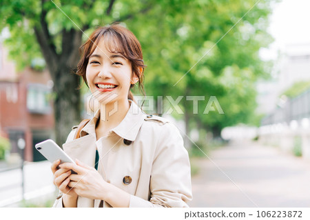 A young woman with a smartphone outdoors 106223872