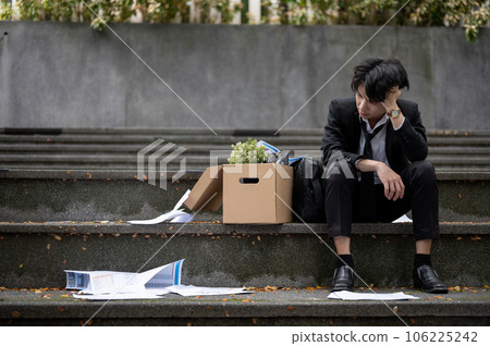 A sad Asian unemployed businessman is sitting on the stairs with a box of his personal stuff 106225242