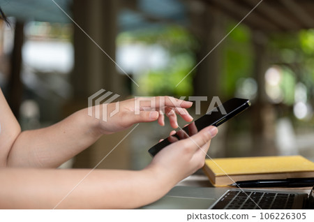 a female using her smartphone at a table while working remotely in a coffee shop. 106226305