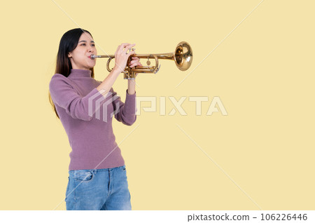 A talented and beautiful Asian woman is playing a trumpet, isolated yellow background A talented and beautiful Asian woman is playing a trumpet, isolated yellow background 106226446
