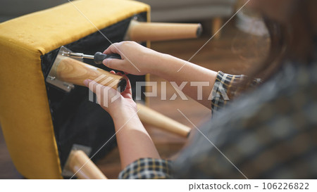 Women tighten screw with screwdriver equipment for assembling leg of chair and making furniture Women tighten screw with screwdriver equipment for assembling leg of chair and making furniture 106226822