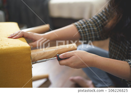 Women tighten screw with screwdriver equipment for assembling leg of chair and making furniture Women tighten screw with screwdriver equipment for assembling leg of chair and making furniture 106226825