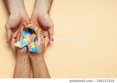 Ribbon with colorful puzzle pieces in hands on light background, place for text. World autism day concept Ribbon with colorful puzzle pieces in hands on light background, place for text. World autism day concept 106227328