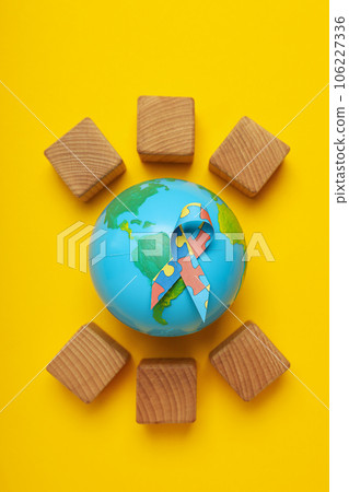 A ribbon with colorful puzzle pieces, cubes and a model of the planet Earth on a light background. World autism day concept 106227336