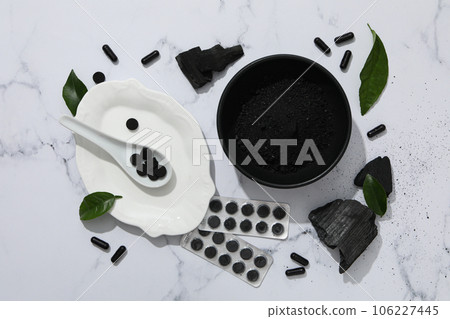 Activated charcoal in tablets and powder in a black bowl 106227445