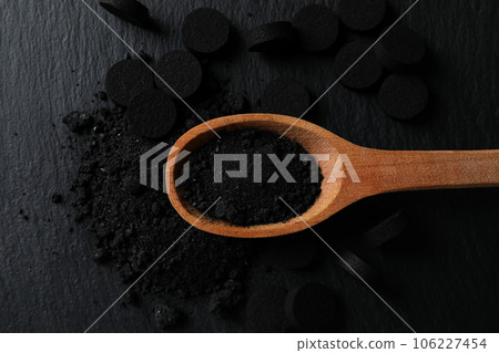 Activated charcoal powder in a wooden spoon on a dark background 106227454