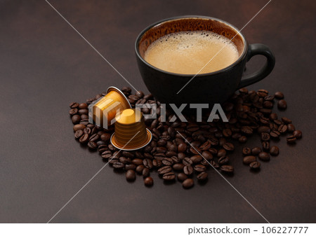 Black coffee in large porcelain cup with raw beans and capsules on brown Black coffee in large porcelain cup with raw beans and capsules on brown 106227777