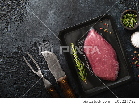 Beef raw fillet steak in vacuum tray with pepper,salt and rosemary on black background 106227782