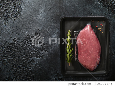 Fresh raw beef fillet steak sealed in vacuum tray with pepper and rosemary on black Fresh raw beef fillet steak sealed in vacuum tray with pepper and rosemary on black 106227783