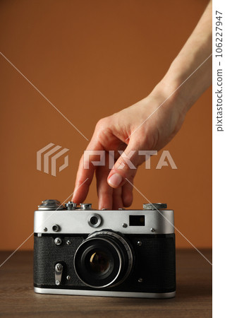 Vintage camera and female hand on wooden table on orange background Vintage camera and female hand on wooden table on orange background 106227947