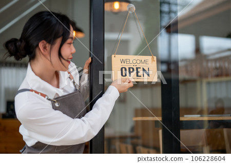 A female restaurant staff or small business owner is hanging an open sign on the entrance door. 106228604