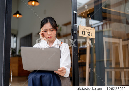 A stressed Asian female coffee shop owner looking at a laptop screen with a serious and sad face. A stressed Asian female coffee shop owner looking at a laptop screen with a serious and sad face. 106228611