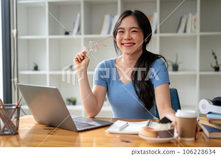 A happy Asian female college student sits at her study table at home. 106228634