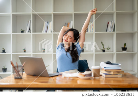 A happy Asian woman stretches her hands at table, enjoying a carefree moment at home after work. 106228635