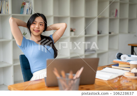 A woman relaxes, puts her hands behind her head, and looks out the window with a happy face 106228637