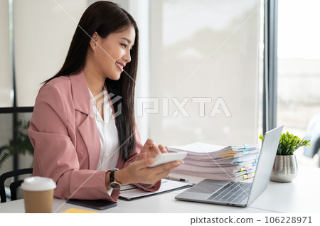 A beautiful Asian businesswoman or female accountant using a calculator at her desk 106228971
