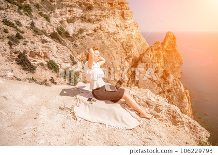 Freelance woman working on a laptop by the sea, typing away on the keyboard while enjoying the beautiful view, highlighting the idea of remote work. Freelance woman working on a laptop by the sea, typing away on the keyboard while enjoying the beautiful view, highlighting the idea of remote work. 106229793