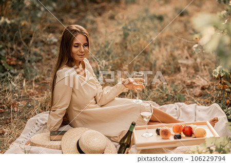 Woman picnic vineyard. Romantic dinner, fruit and wine. Happy woman with a glass of wine at a picnic in the vineyard on sunny day, wine tasting at sunset. Woman picnic vineyard. Romantic dinner, fruit and wine. Happy woman with a glass of wine at a picnic in the vineyard on sunny day, wine tasting at sunset. 106229794