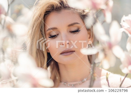 Portrait of a beautiful happy middle aged woman enjoying the smell in a blooming spring garden. Beautiful magnolia bushes, large flowers. 106229796