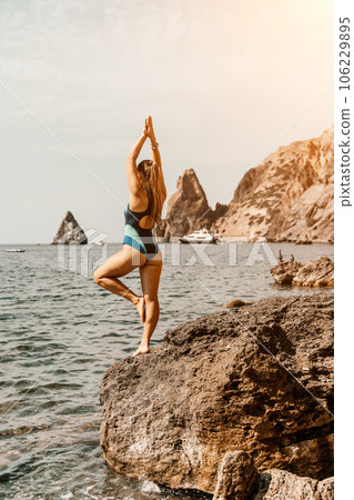 Yoga on the beach. A happy woman meditating in a yoga pose on the beach, surrounded by the ocean and rock mountains, promoting a healthy lifestyle outdoors in nature, and inspiring fitness concept. 106229895