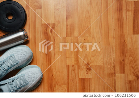 New light blue green female running shoes metal water bottle and weight plate on emty wooden floor. Stylish monochrome shoes for active people that incorporate new health technology. Top view 106231506