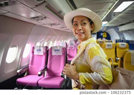 Smiling middle age female tourist with bag walking the aisle on plane. Retirement, travel and summer vacation concept 106232375