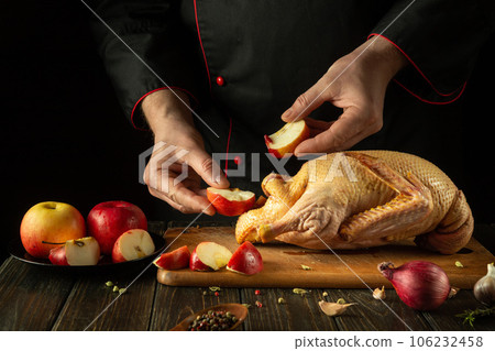 Cooking duck with apples and spices for lunch by the chef's hands. Raw duck on the kitchen table and cutting board. Working environment in a restaurant kitchen Cooking duck with apples and spices for lunch by the chef's hands. Raw duck on the kitchen table and cutting board. Working environment in a restaurant kitchen 106232458