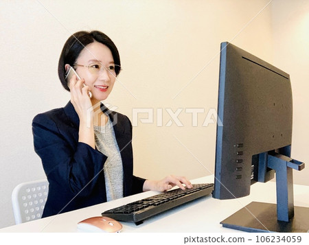 A woman operating a computer while talking on a smartphone A woman operating a computer while talking on a smartphone 106234059