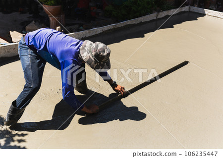 Workers level cement concrete concrete patio floor using long trowel. Workers level cement concrete concrete patio floor using long trowel. 106235447