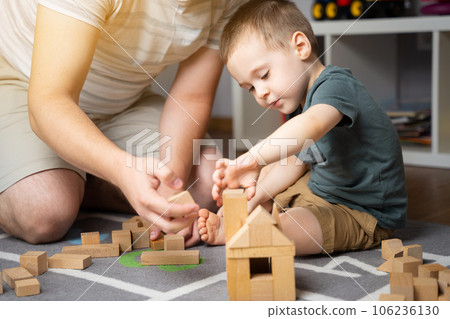 Little toddler boy 2,5 years playing wooden blocks with dad. Spending time with children. Educational activities for kids. Children's room. Indoors. Selective focus Little toddler boy 2,5 years playing wooden blocks with dad. Spending time with children. Educational activities for kids. Children's room. Indoors. Selective focus 106236130