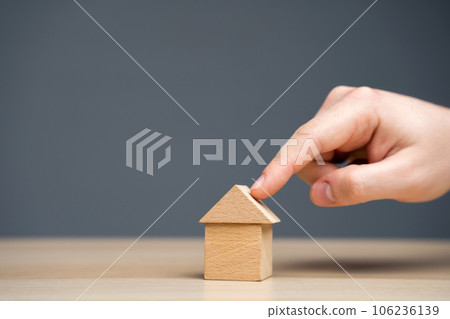 The man points to a miniature house. The concept of real estate and affordable housing. Mortgage rates and loans. Sale, purchase and rent of apartments. Taxes, utilities and insurance 106236139