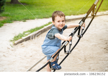 Happy toddler boy 2.5 years old climbs the rope ladder at the playground in the park. Active games and entertainment for children. sunny summer day Happy toddler boy 2.5 years old climbs the rope ladder at the playground in the park. Active games and entertainment for children. sunny summer day 106236152