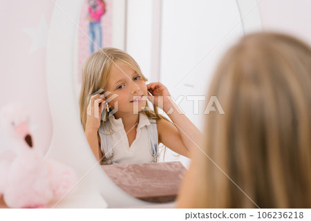 Happy child girl of seven years old puts on earrings in front of the mirror 106236218