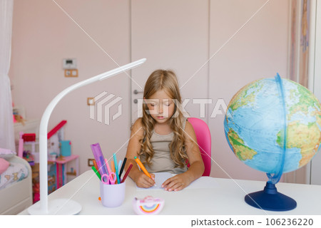 Girl sits at home at a table and write in a notebook, completing a learning task or repeating lessons at home Girl sits at home at a table and write in a notebook, completing a learning task or repeating lessons at home 106236220