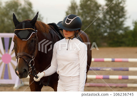 Jockey female rider in uniform holds bridle of dressage horse during equestrian jumping competition show Jockey female rider in uniform holds bridle of dressage horse during equestrian jumping competition show 106236745