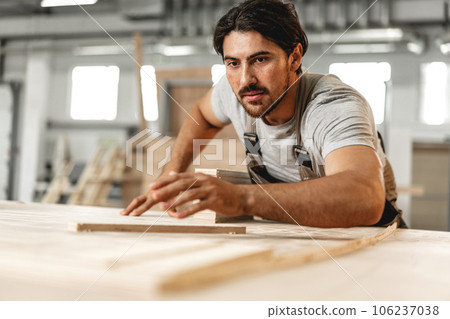 Young carpenter man looking and choosing wood plank at workshop in carpenter wood factory Young carpenter man looking and choosing wood plank at workshop in carpenter wood factory 106237038