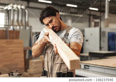 Young carpenter man looking and choosing wood plank at workshop in carpenter wood factory 106237046