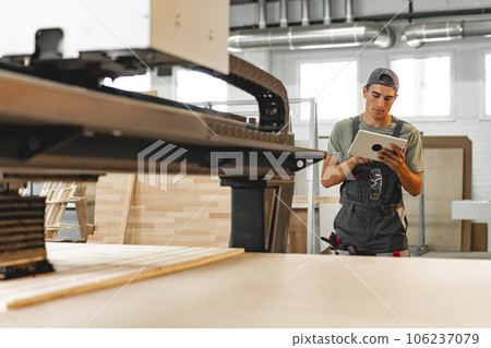 Young carpenter operating machine for wood processing at a furniture factory 106237079