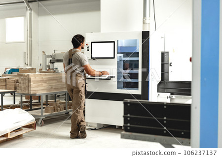 Young carpenter operating machine for wood processing at a furniture factory 106237137