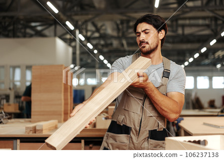 Young carpenter man looking and choosing wood plank at workshop in carpenter wood factory 106237138