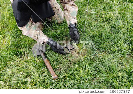 A man in a military uniform and a bulletproof vest works in the forest to demine the territory. A man defuses an anti-personnel mine A man in a military uniform and a bulletproof vest works in the forest to demine the territory. A man defuses an anti-personnel mine 106237577