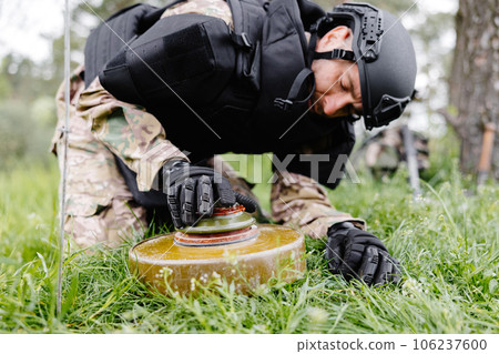 A man in a special suit works with a detector and found an explosive device. A man tries to neutralize an anti-tank mine 106237600
