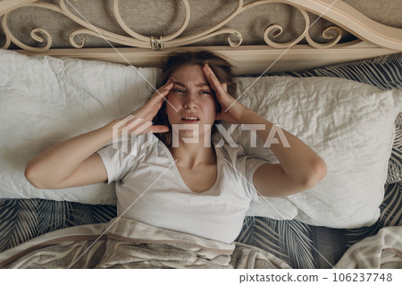 Young woman with headache flu ill sick disease cold at home indoor lying on bed 106237748