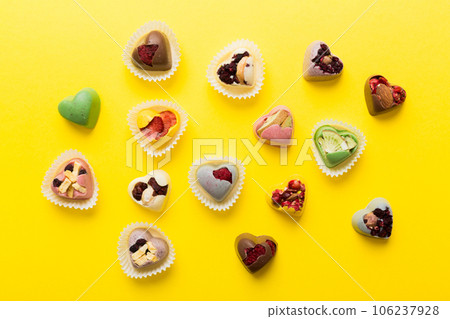 chocolate sweets in the form of a heart with fruits and nuts on a colored background. top view with space for text, holiday concept chocolate sweets in the form of a heart with fruits and nuts on a colored background. top view with space for text, holiday concept 106237928