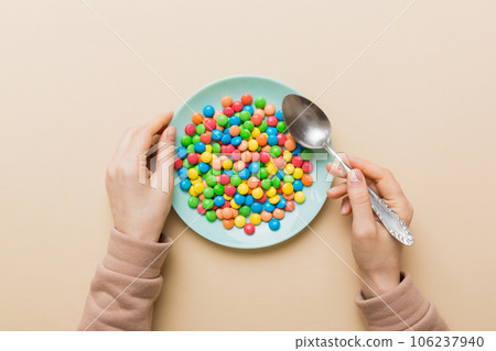 the girl holds cutlery in her hands and eats sweets in a plate. Health and obesity concept, top view on colored background 106237940