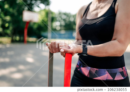 Young girl woman exercising outdoors with rubber elastic band doing training for her hands. Closeup view of active fitness with additional sport equipment outside Young girl woman exercising outdoors with rubber elastic band doing training for her hands. Closeup view of active fitness with additional sport equipment outside 106238055