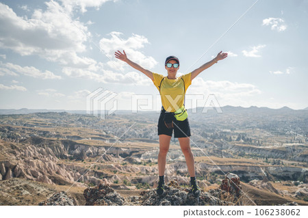 Woman tourist with backpack standing on mountain top in Cappadocia with open arms, Turkey Woman tourist with backpack standing on mountain top in Cappadocia with open arms, Turkey 106238062
