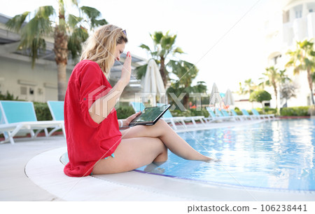 Woman happily greets with hand business partners on tablet while sitting in pool 106238441