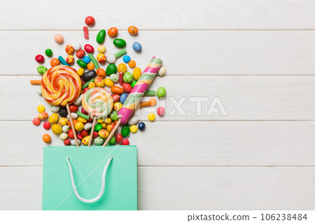 shopping paper gift bag in corner full of assorted traditional candies falling out on colored background with copy space. Happy Holidays sale concept shopping paper gift bag in corner full of assorted traditional candies falling out on colored background with copy space. Happy Holidays sale concept 106238484